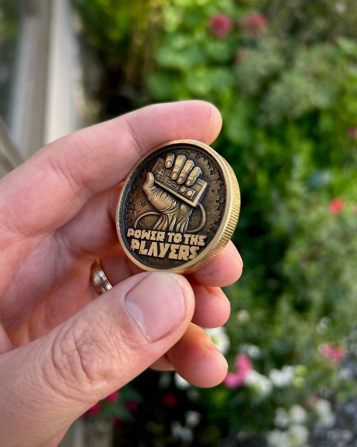 Angled view of the gaming coin showing the engraved controller, gripping hand and raised lettering against a dark textured background.
