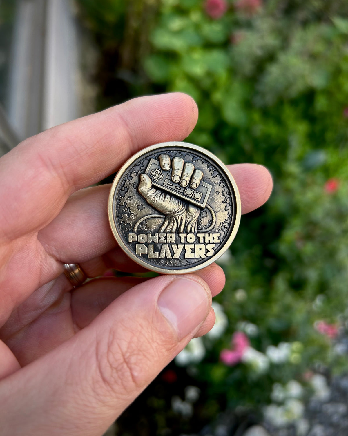 Retro gamer EDC coin held in a hand, featuring a fist gripping a wired controller above the raised words “Power to the Players.