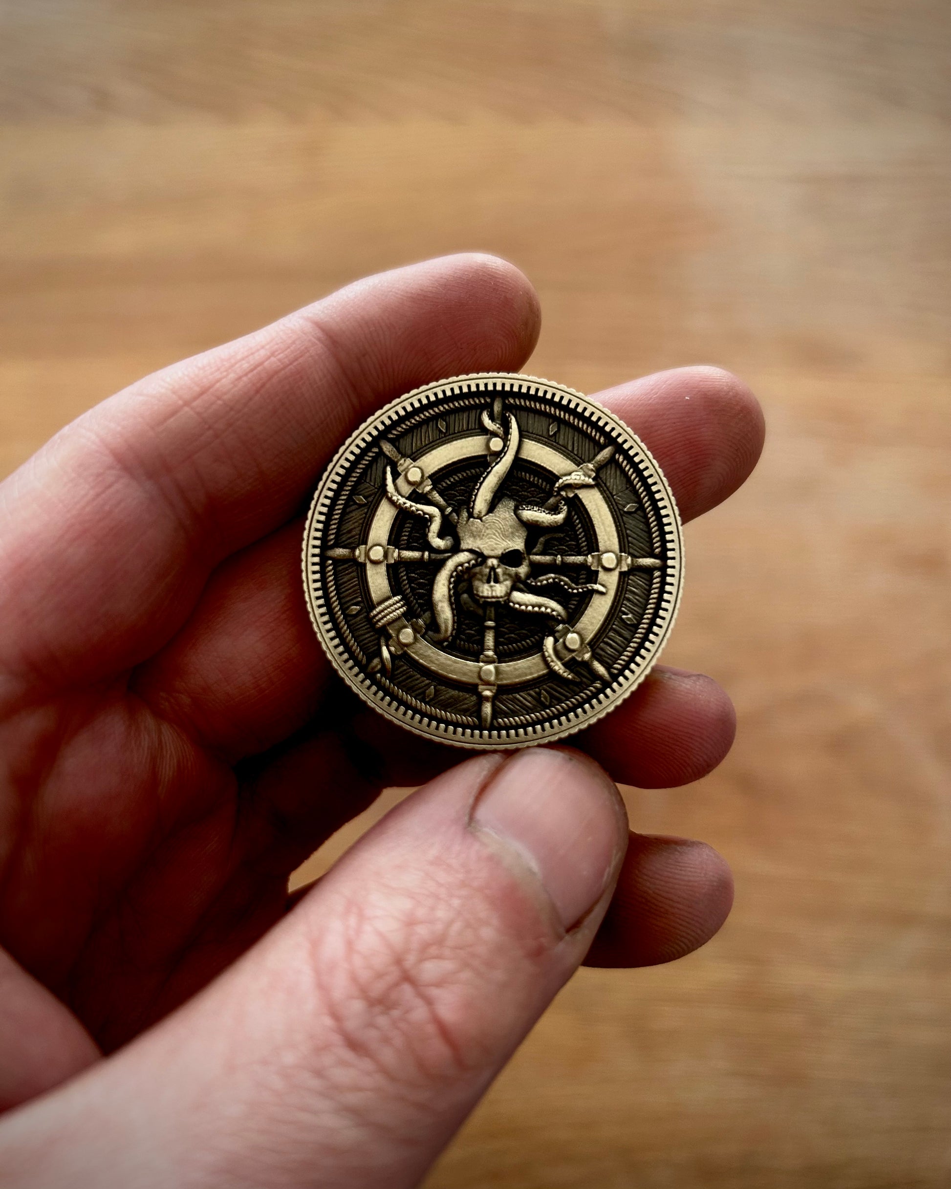 Hand holding a brass coin with a detailed pirate themed design against a wooden background