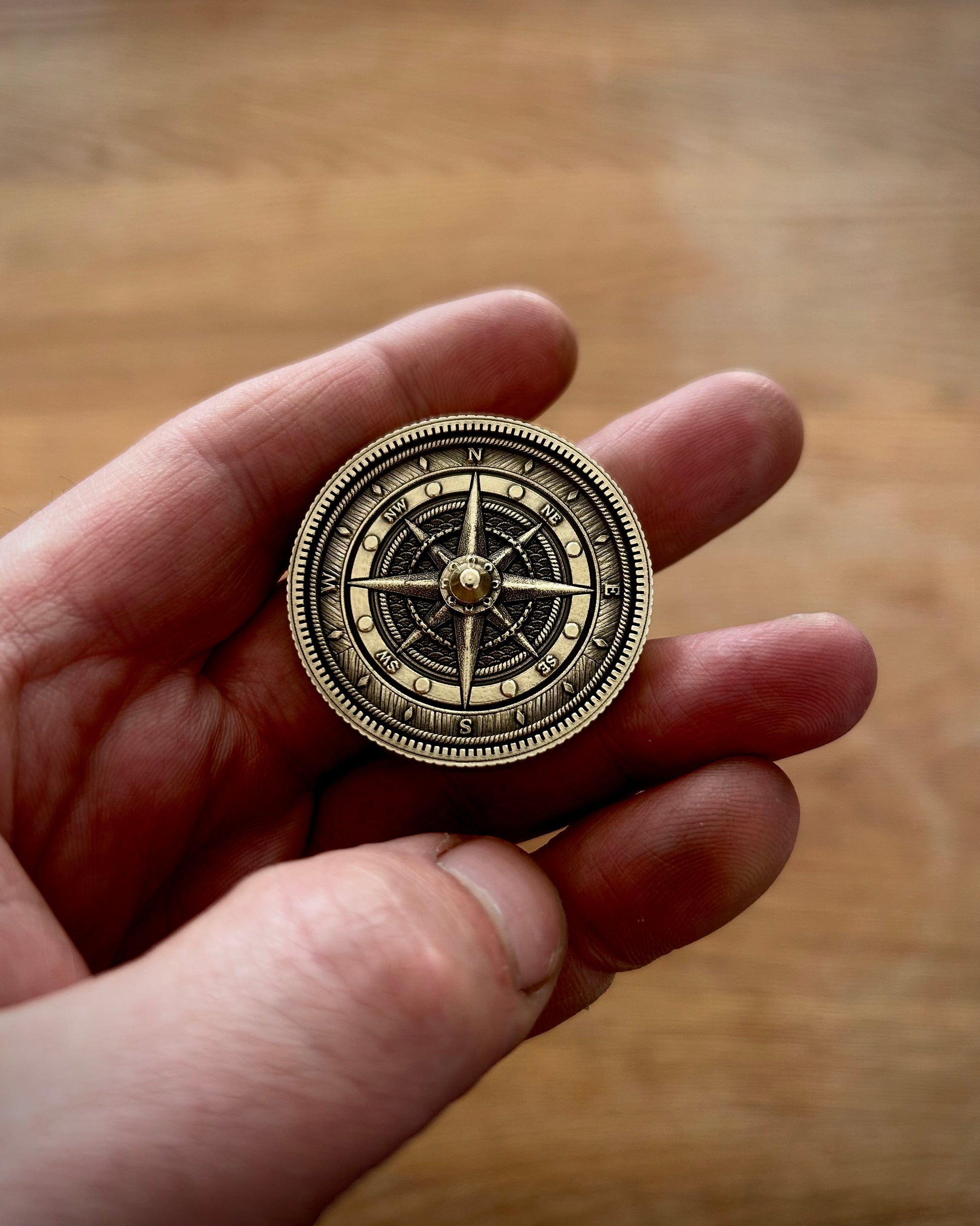 Hand holding a brass compass spinner coin against a wooden background