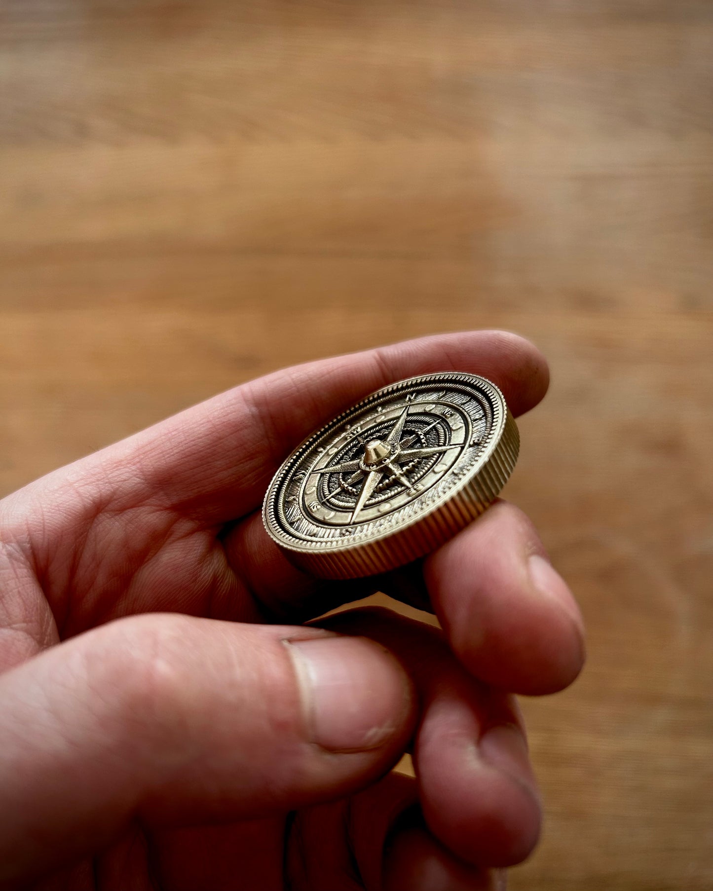 Hand holding a gold compass against a wooden background