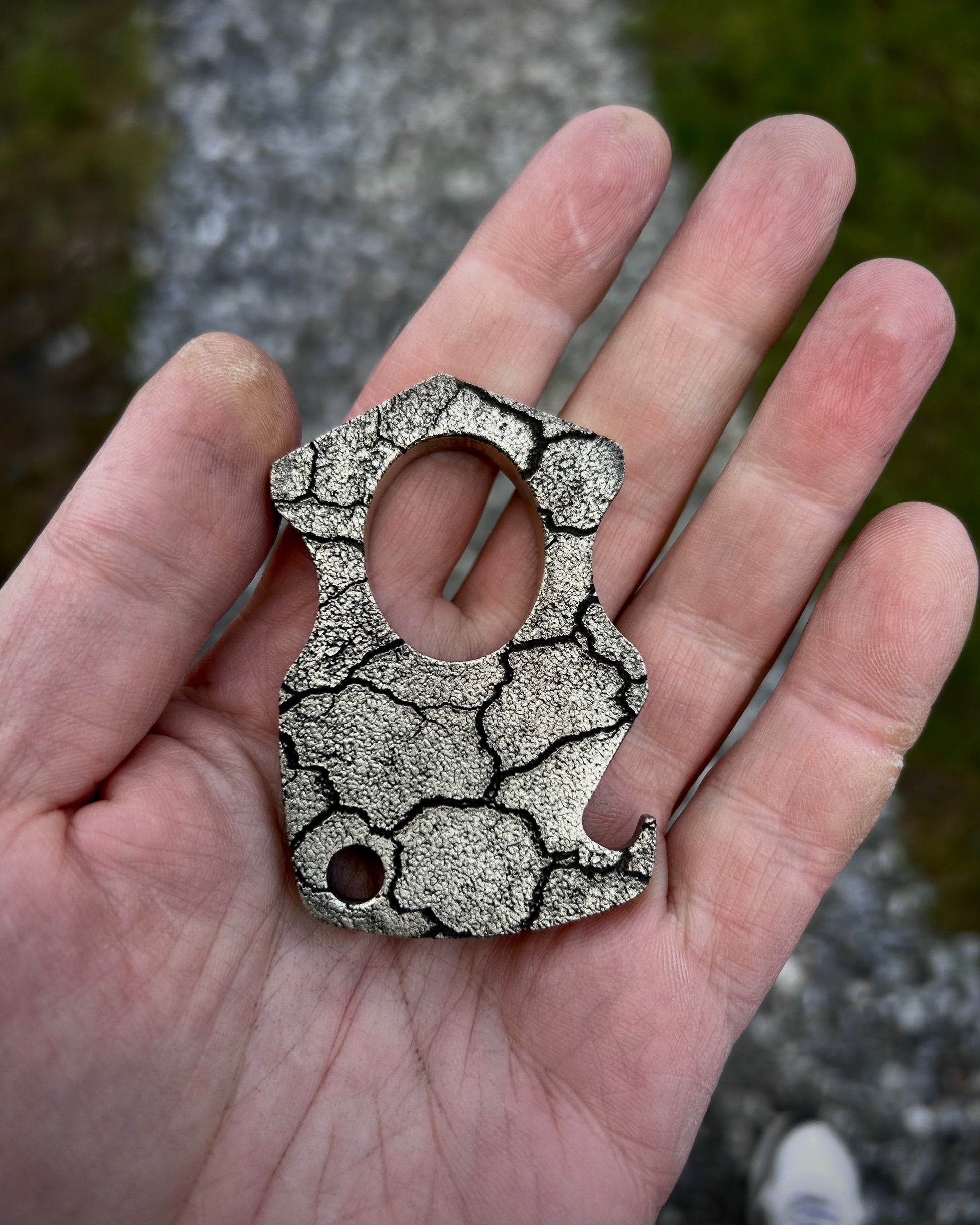 Hand holding a silver textured brass bottle opener against a natural background