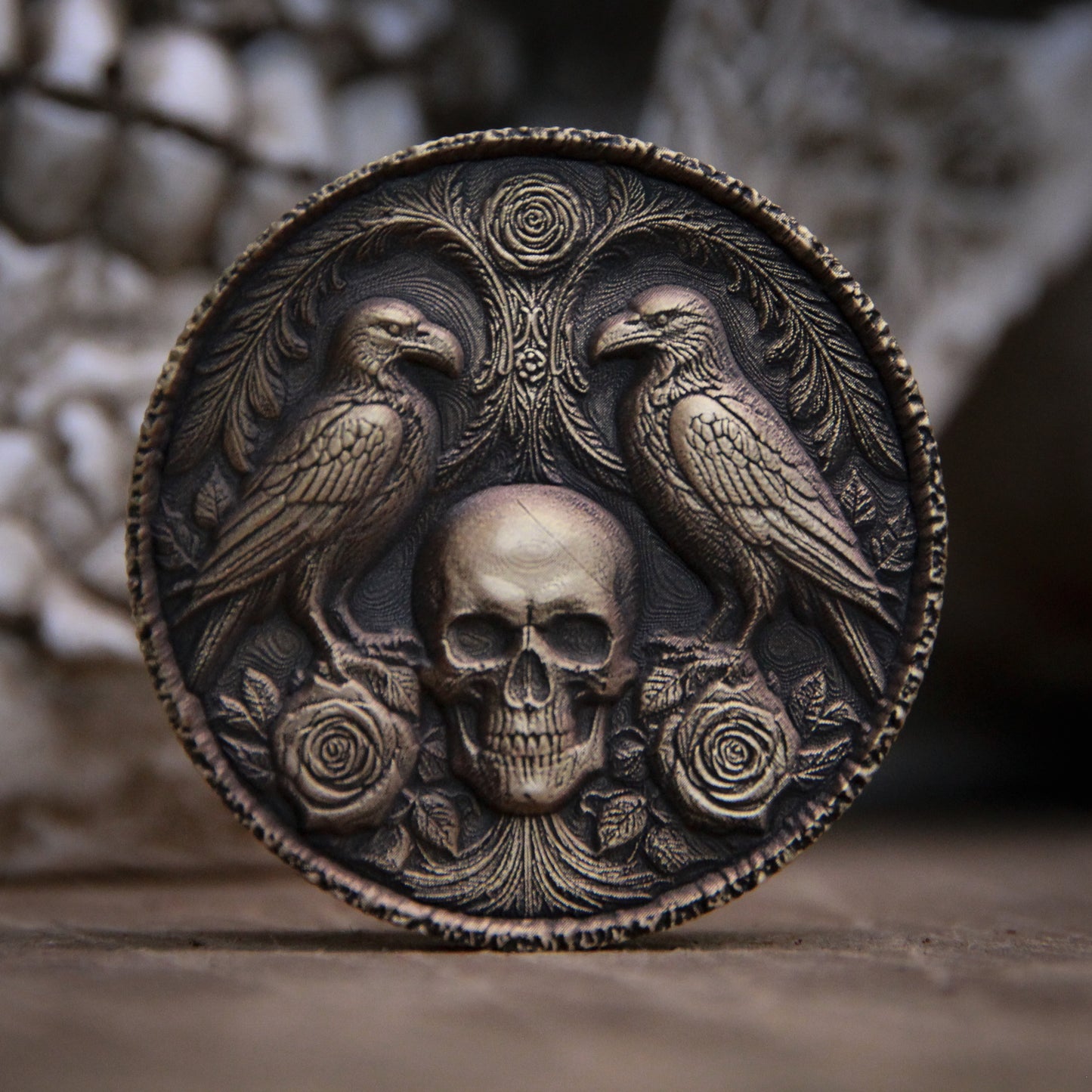 Decorative coin with skull and ravens design on a textured surface