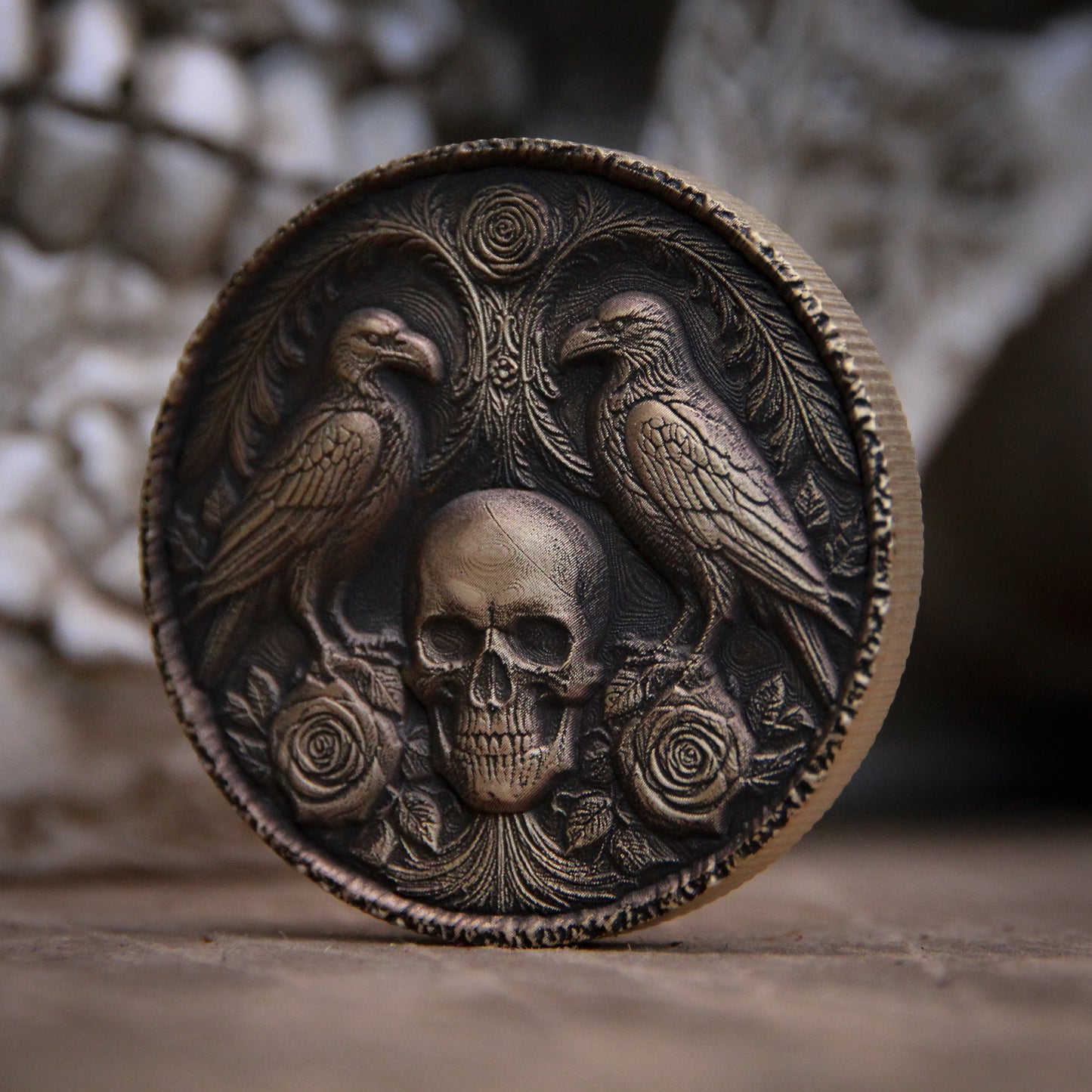Bronze coin with embossed design of a skull and two birds on a textured surface