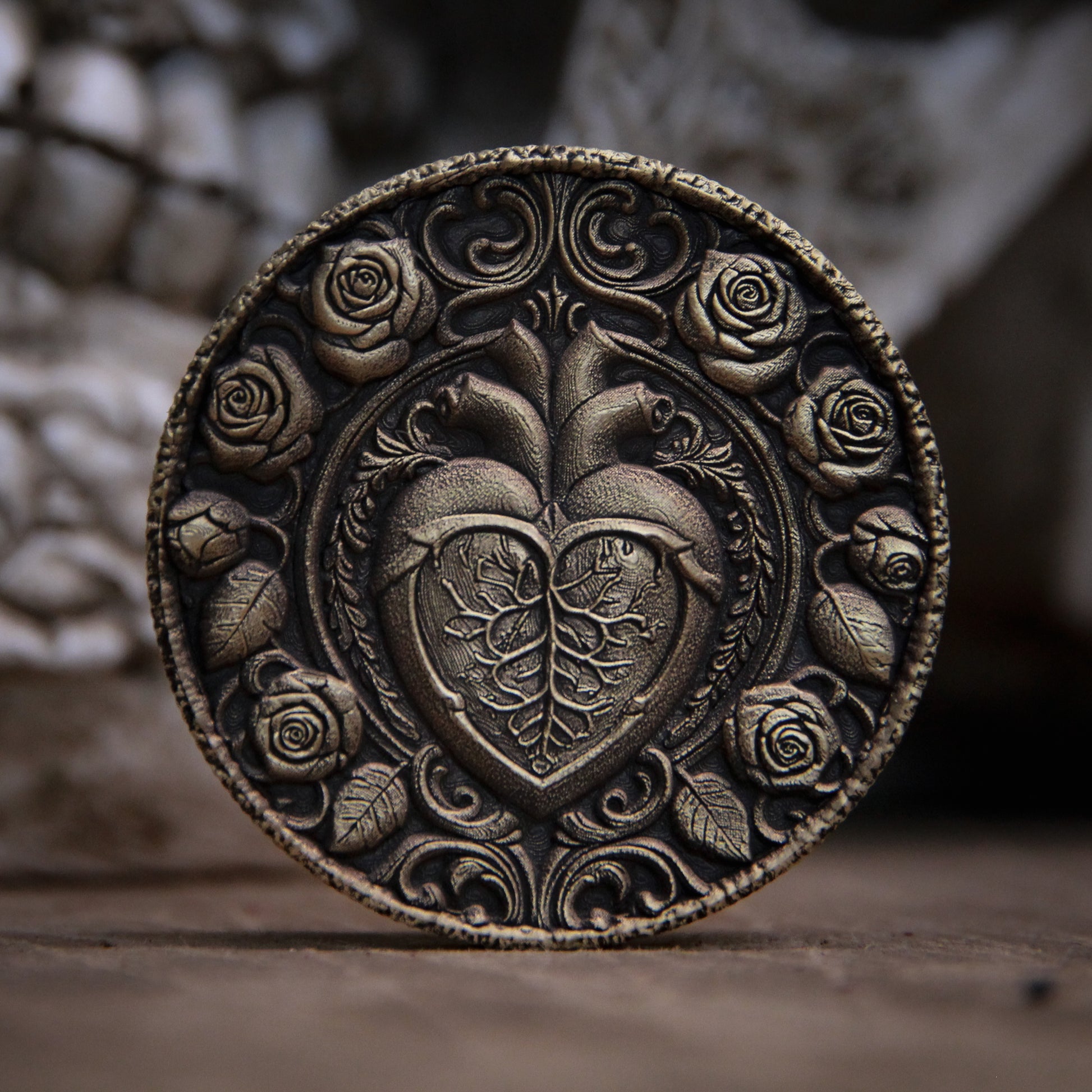 Decorative metal coin with heart and rose design on a textured surface
