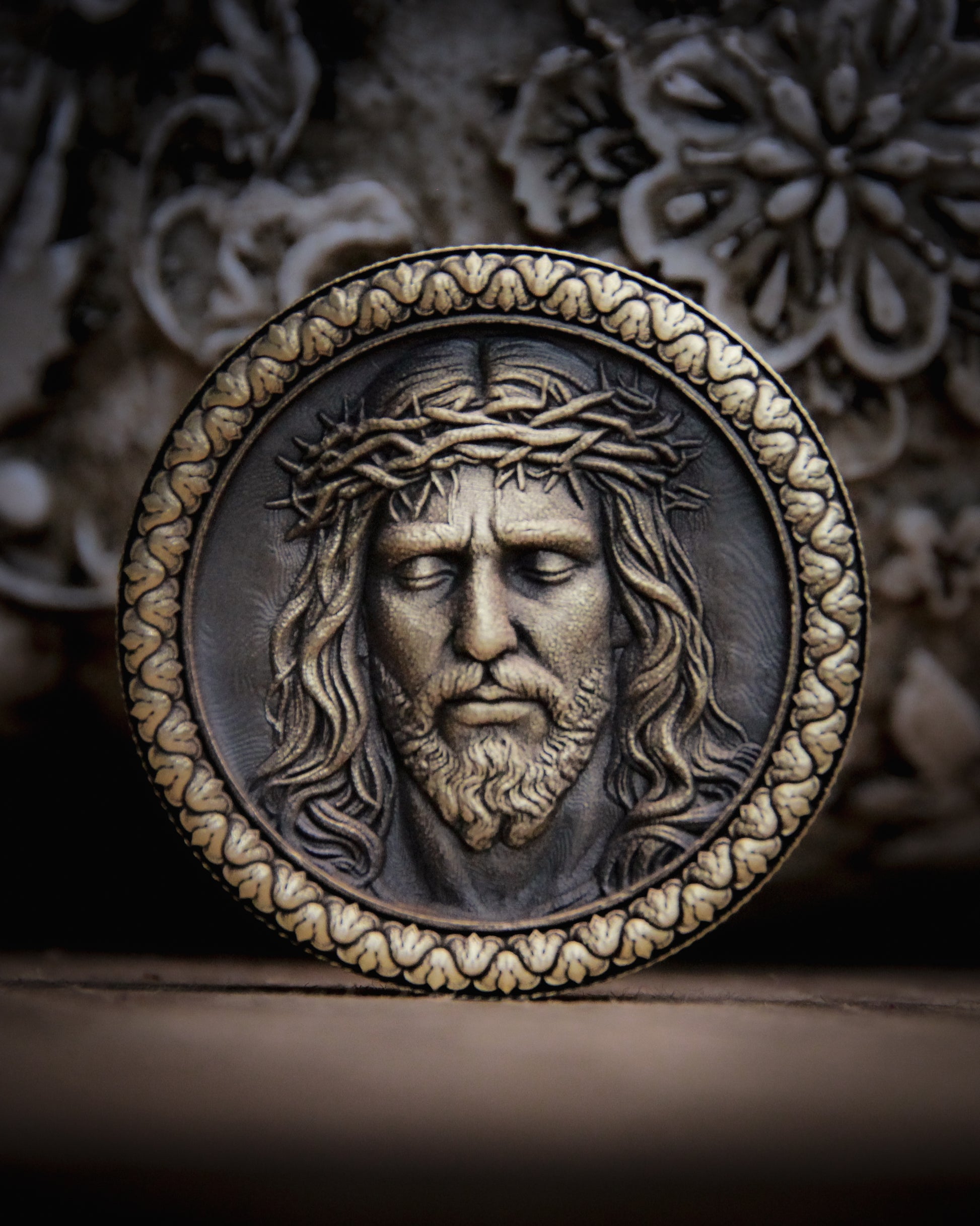 Medallion with embossed face of Jesus Christ wearing a crown of thorns on a textured background.