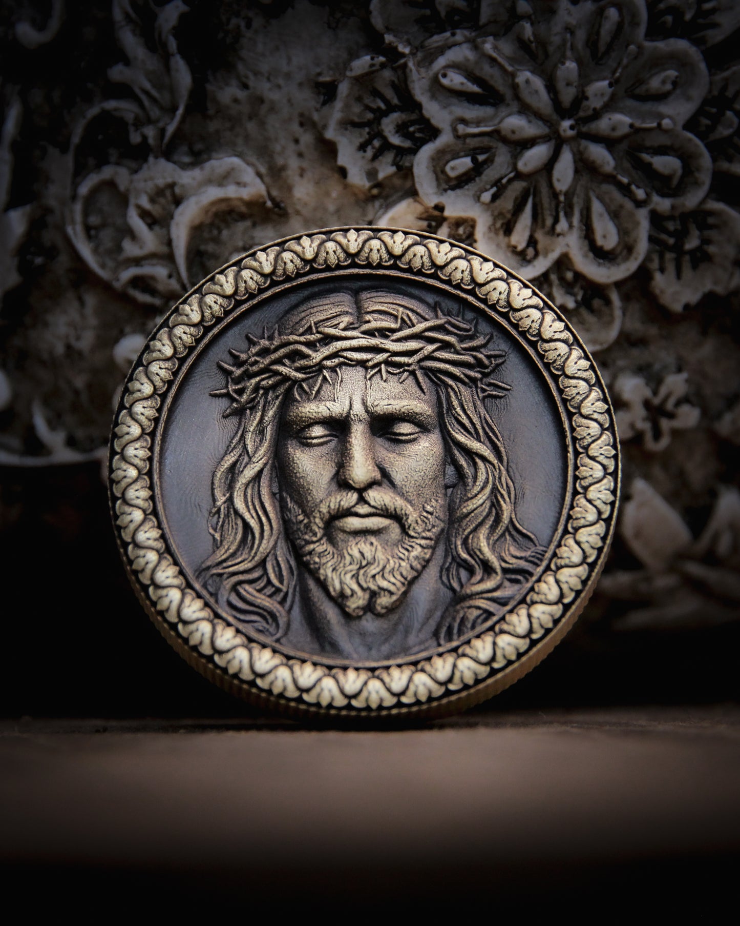 Medallion with embossed face of Christ on a dark floral background