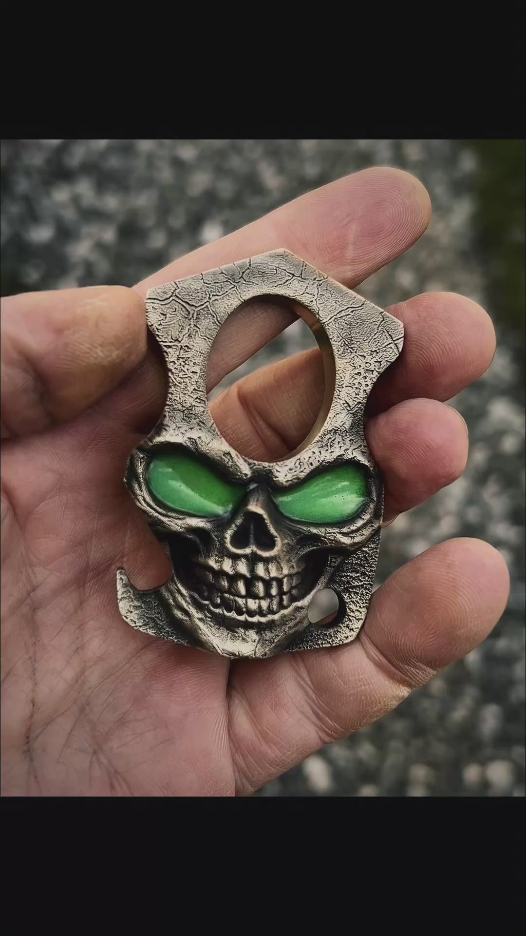 Skull-shaped bottle opener with green glow in the dark eyes held in a hand against a natural background