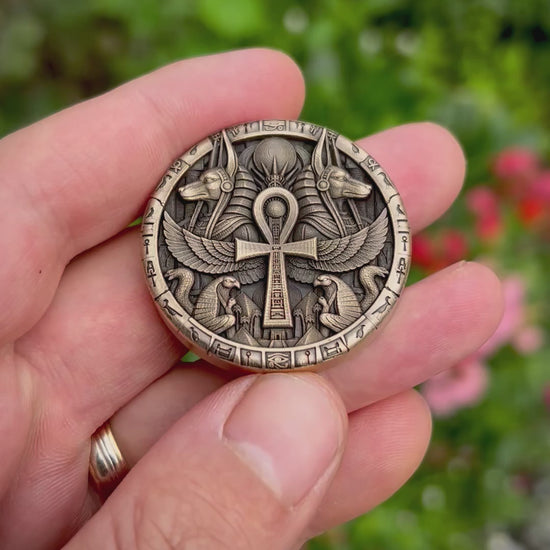 Close-up video of the coin’s reverse, showing a winged ankh, paired Anubis heads, falcons and serpents, with angled views revealing the engraving depth and polished highlights.