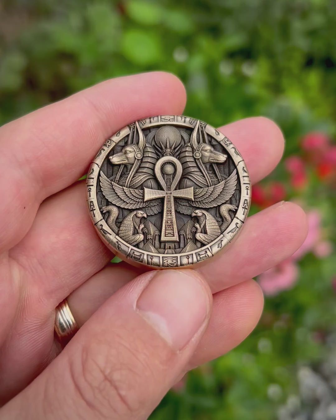 Close-up video of the coin’s reverse, showing a winged ankh, paired Anubis heads, falcons and serpents, with angled views revealing the engraving depth and polished highlights.