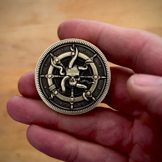 Hand holding a brass coin with a detailed pirate themed design against a wooden background