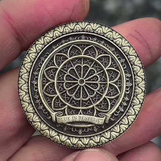 Decorative metal coin one side with saint Michael and the other side with intricate design and 'Lux in Tenebris' text on a wooden surface.