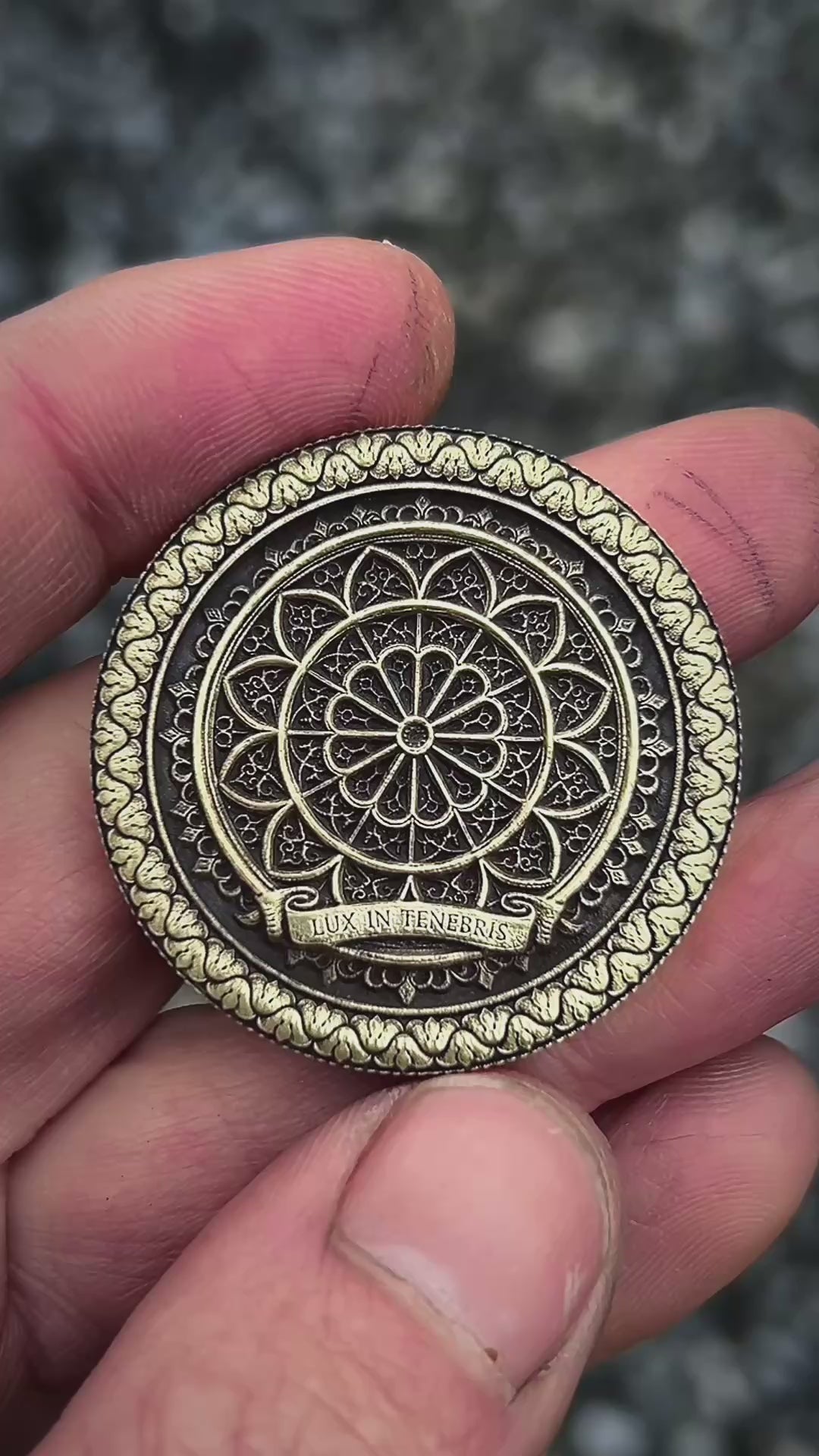 Decorative metal coin one side with saint Michael and the other side with intricate design and 'Lux in Tenebris' text on a wooden surface.